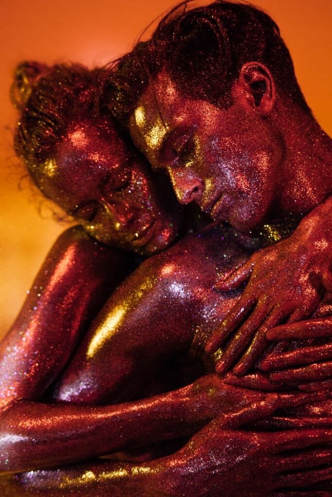 A captivating shot of two models embracing with glittery body paint under warm lighting.