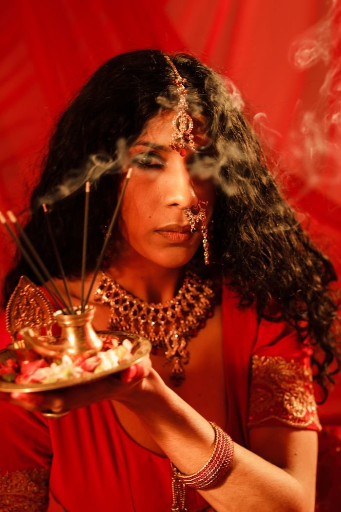 A close-up portrait of an Indian woman in traditional attire holding incense with intricate jewelry.